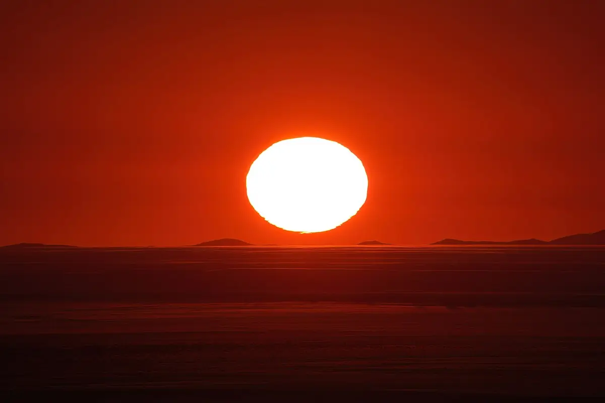 Image B: A glowing sun setting into a flat horizon under a deep red sky in the Namib desert